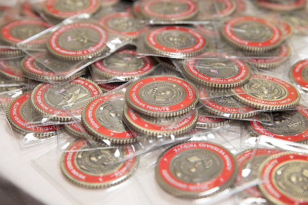 Challenge coins from the Alumni Veterans Tribute dedication on a table.