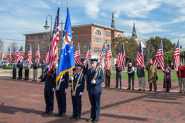 A ROTC color guard stands in front of veterans holding flags at a parade.