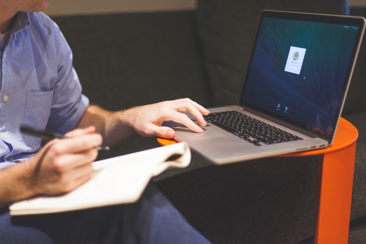 A man working on his laptop while writing on a note pad