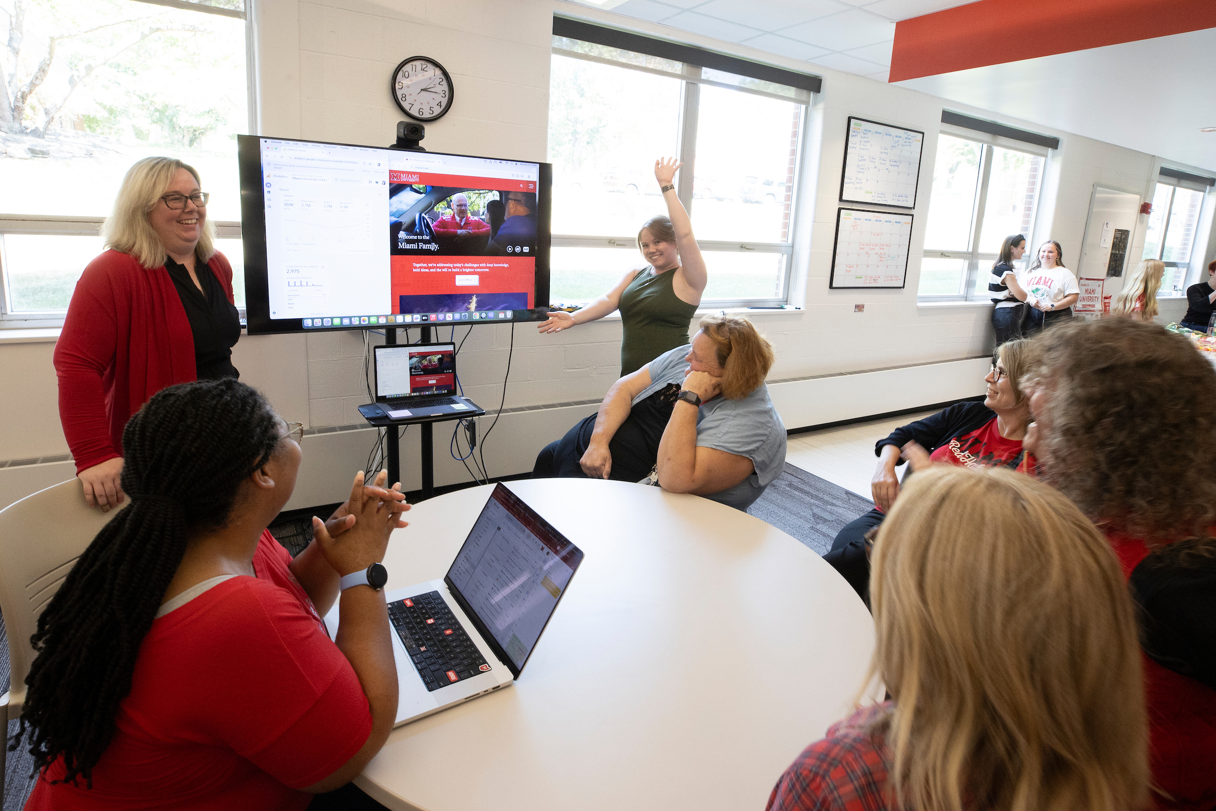 Miami staff members work together on a project, with two presenting to their seated colleagues.