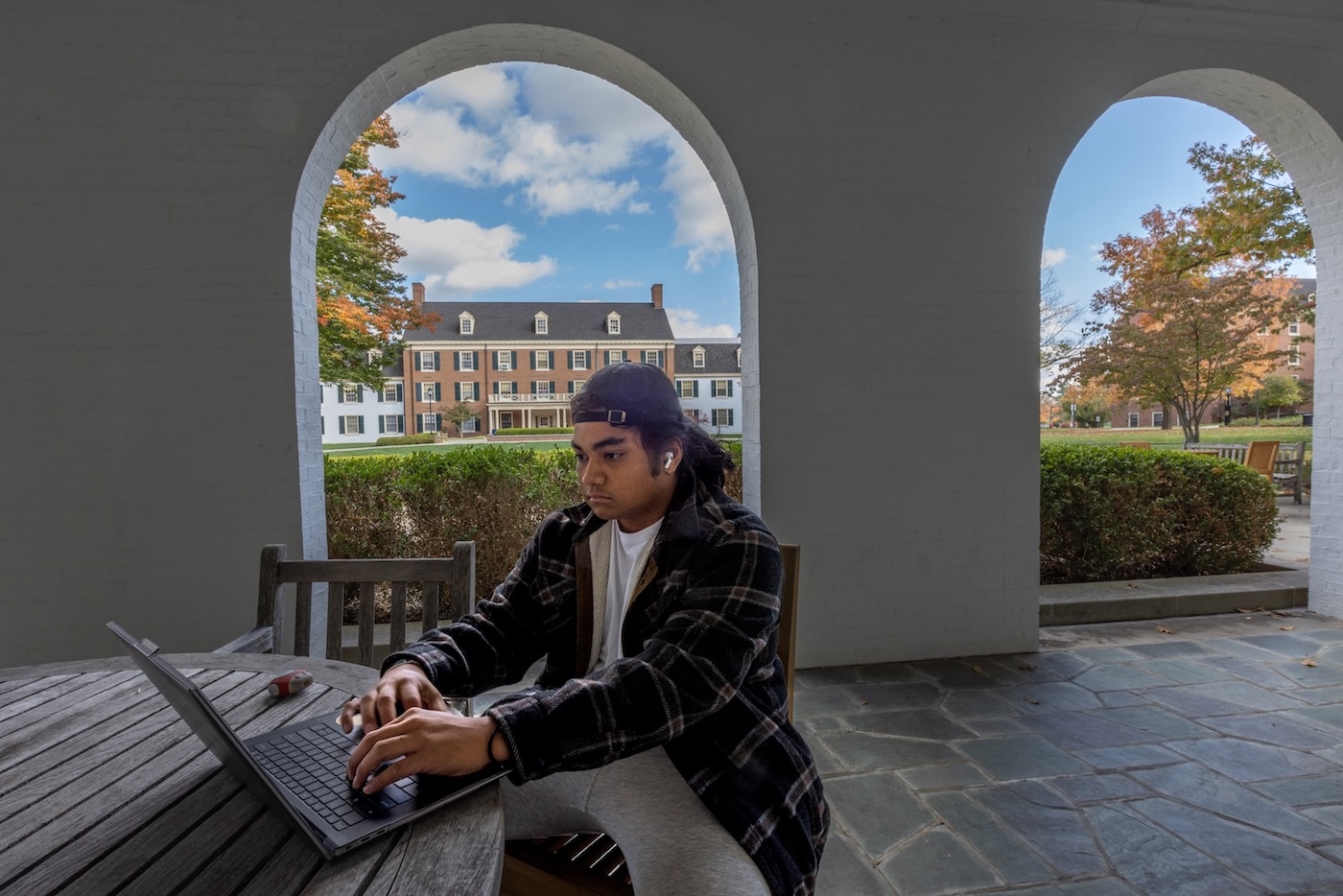 A student sending in a residence hall portico working on a laptop