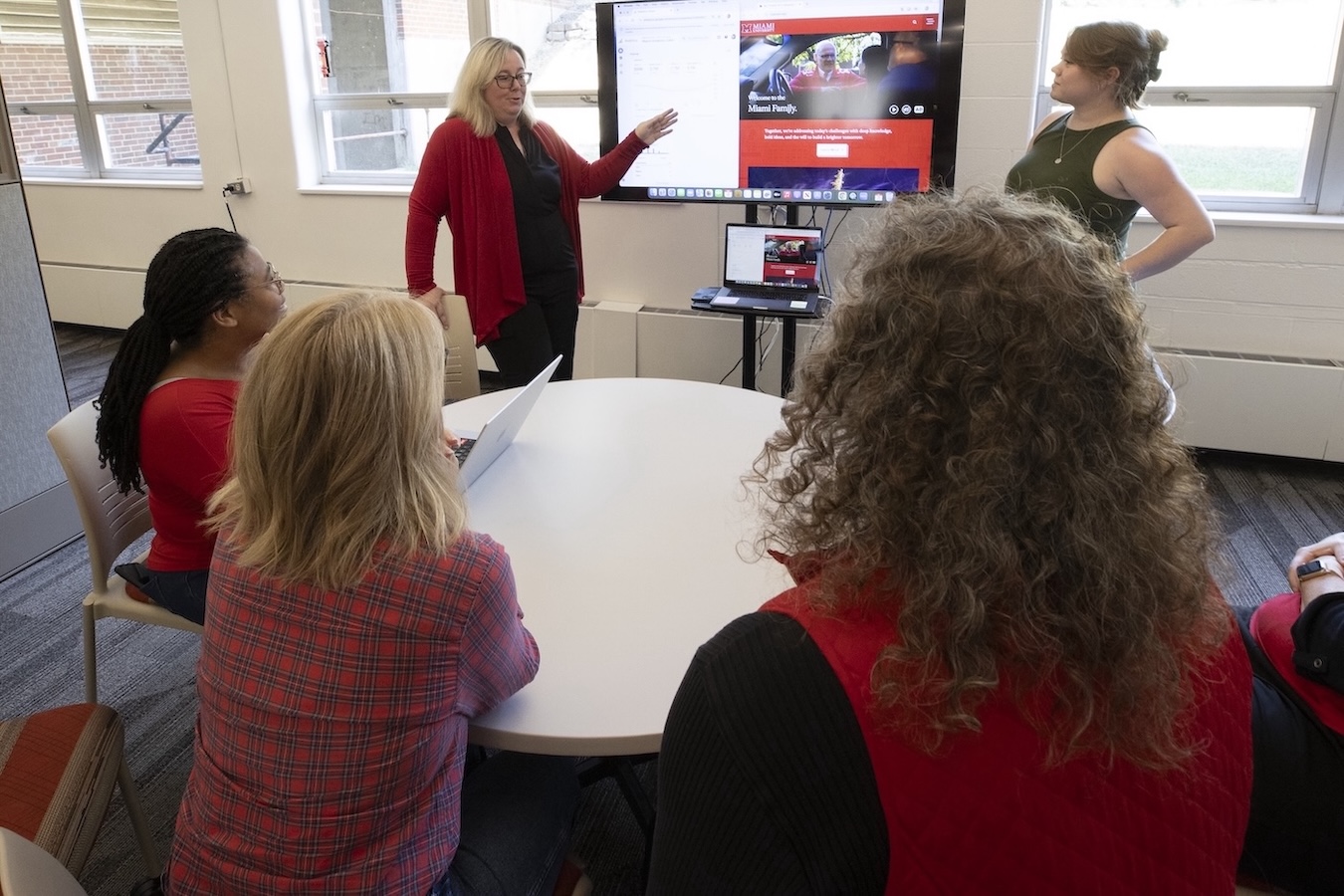 A group of Miami employees sitting around a table, watching a presentation given by another employee using a large display screen