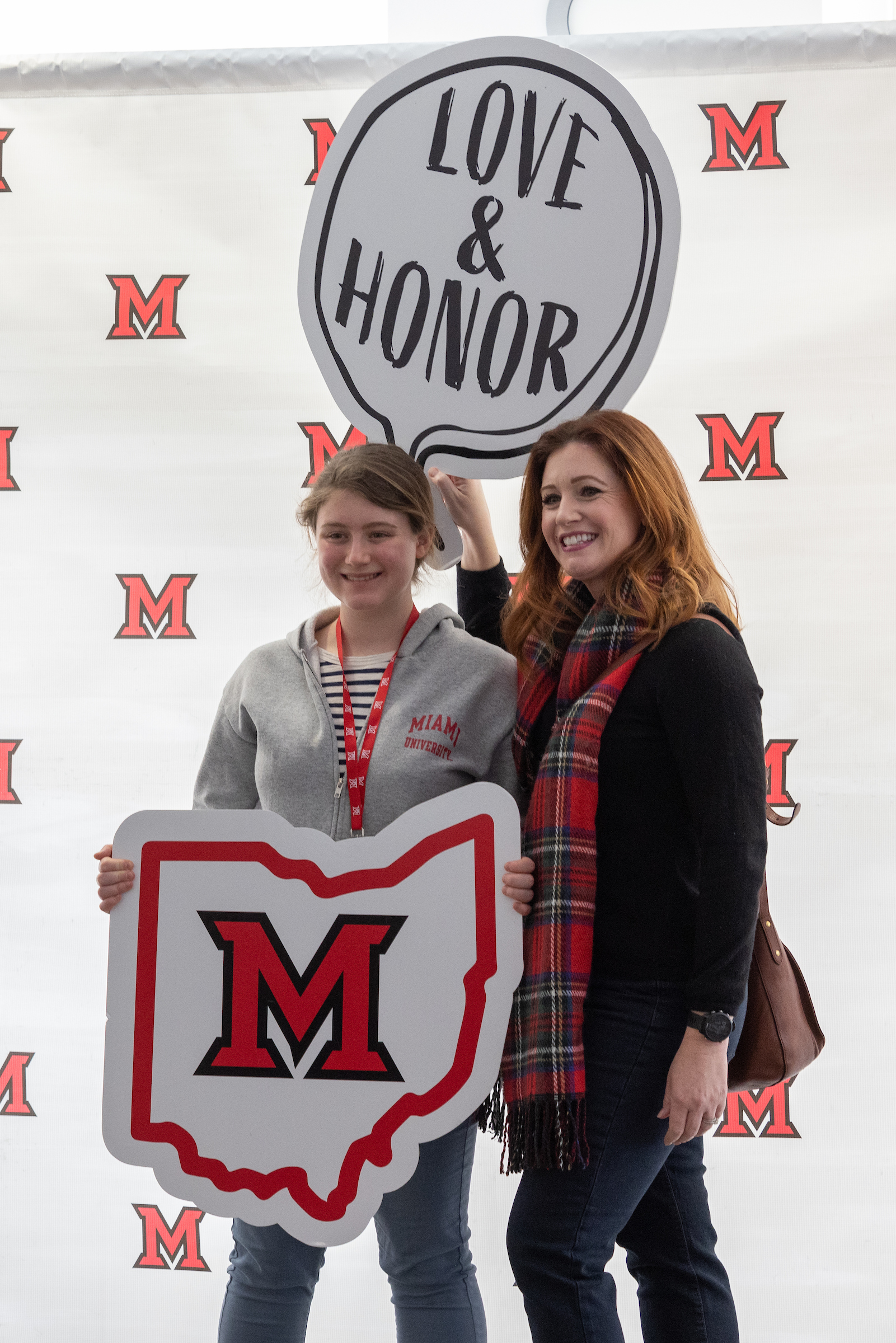 A student and parent pose for a picture with a sign reading Love and Honor.