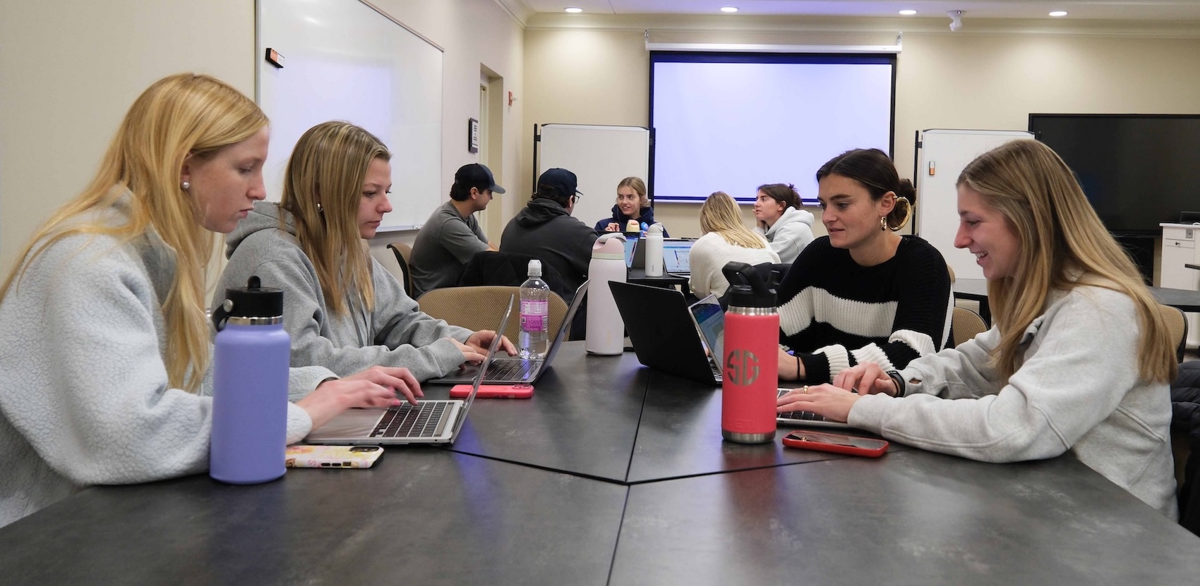 A group of students sitting at a long table working on their laptops