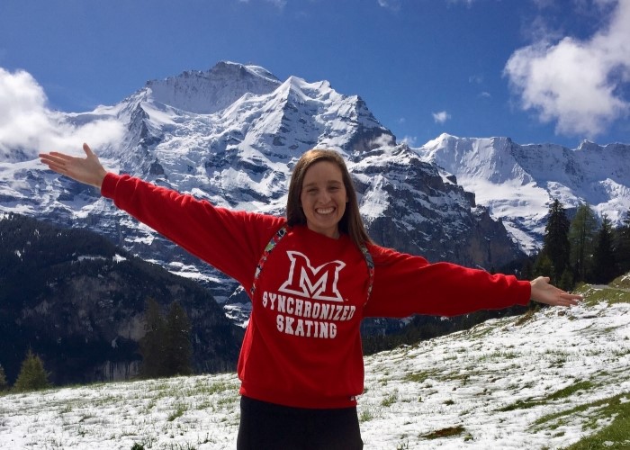 Miami student wearing a synchronized skating hoodie stands in front of a massive snowy mountain